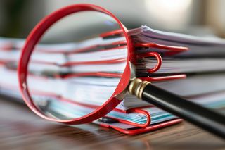 Foto: Lupe vor Dokumentenstapel